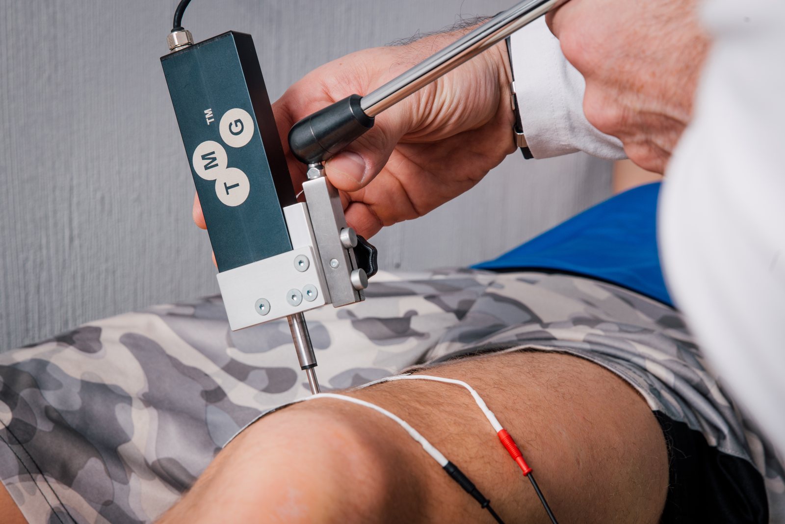Close-up: Tomaž Brinec's hands positioning the TMG sensor between two electrodes on an athlete's thigh.